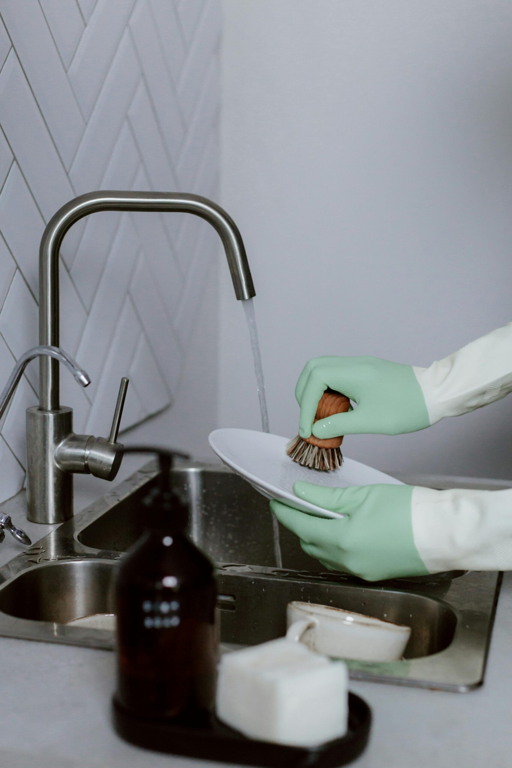 Person with gloves and sponge washing a foamy dinner plate